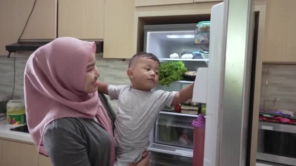 Muslimische Mutter trägt ihren Sohn und öffnet den Kühlschrank — Stockvideo
