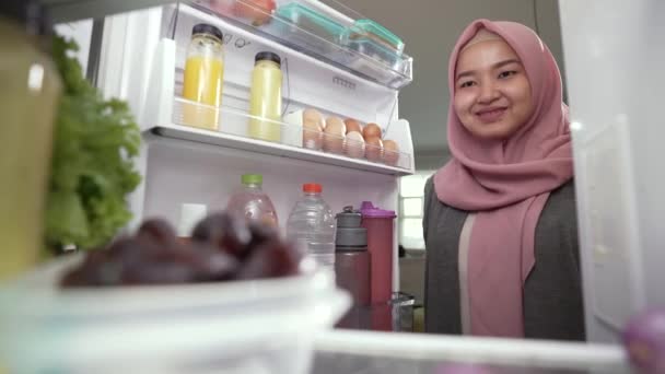 Мусульманская женщина ест фрукты перед холодильником — стоковое видео