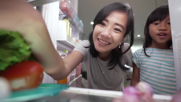 Mamma och hennes dotter har mellanmål tillsammans i köket öppna kylen — Stockvideo