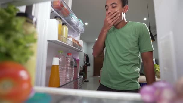 Durstiger junger Mann nimmt ein Getränk in den Kühlschrank und trinkt es — Stockvideo