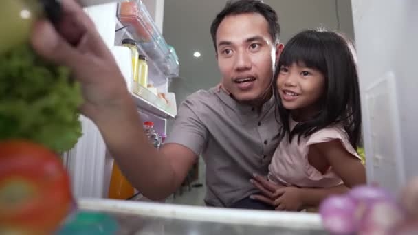 Ο πατέρας και η κόρη της τρώγοντας μαζί στην κουζίνα ανοίγουν το ψυγείο. — Αρχείο Βίντεο