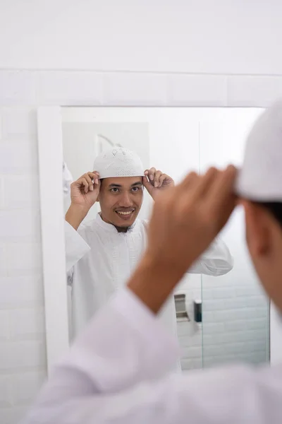Homem muçulmano olhando para o espelho e se vestir usando chapéu islâmico ou boné — Fotografia de Stock