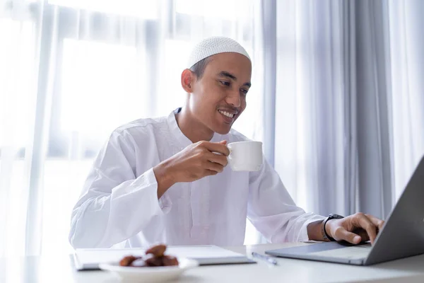 家庭でノートパソコンを使ってコーヒーを飲んでいるイスラム教徒の男性は — ストック写真
