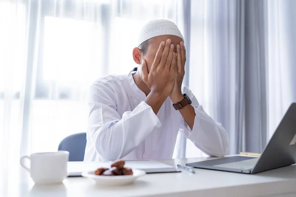 Muslimischer Mann mit Laptop verdeckt sein Gesicht während der Arbeit von zu Hause aus mit der Hand — Stockfoto