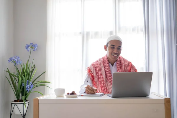 机の上に座りながらノートパソコンを使って仕事をするイスラム教徒のビジネスマン — ストック写真