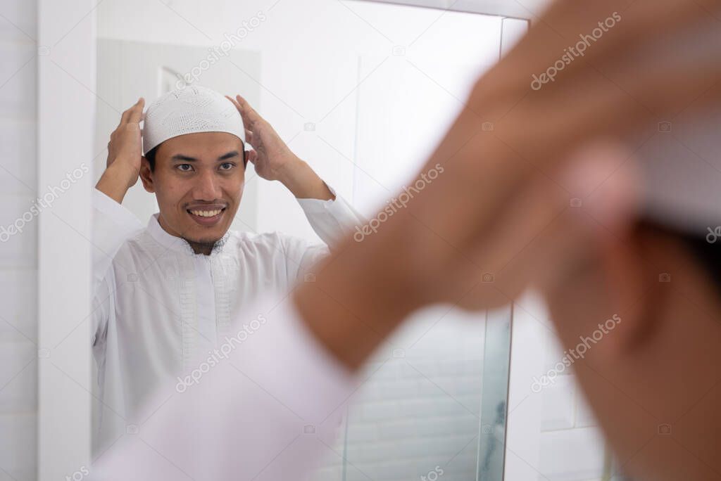 muslim man looking at mirror and get dressed wearing islamic hat or cap