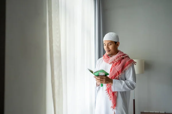 Relijius membaca koran atau quran sambil berdiri di samping jendela — Stok Foto
