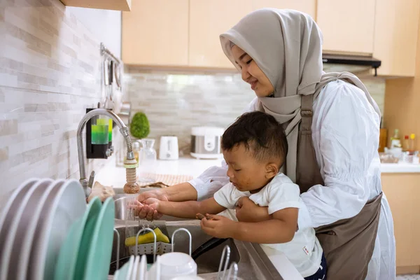 Muslim ibu mencuci tangan anaknya di wastafel dapur — Stok Foto