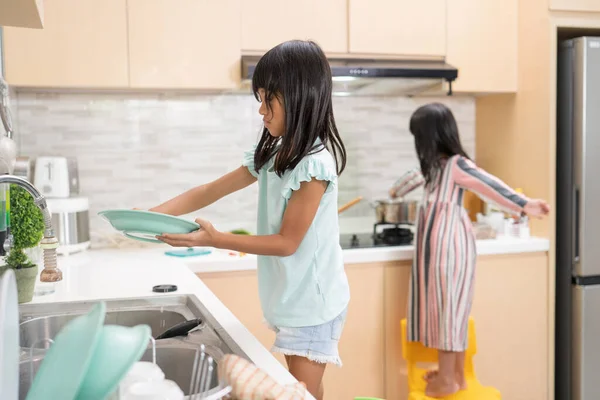 Chica joven feliz están haciendo lavavajillas juntos en el fregadero de la cocina — Foto de Stock
