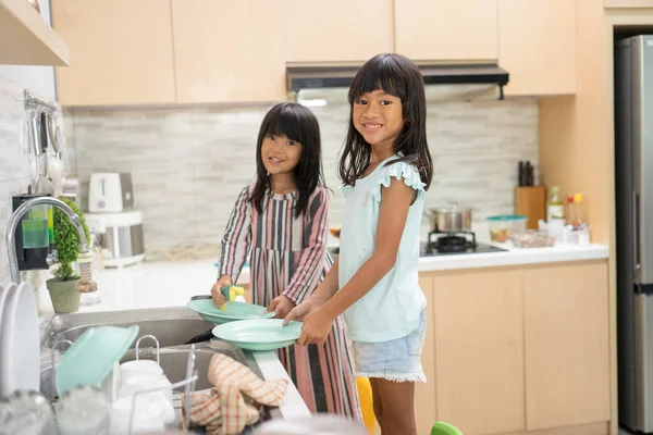 Chica joven feliz están haciendo lavavajillas juntos en el fregadero de la cocina — Foto de Stock