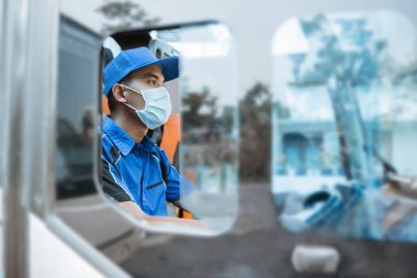 Üniformalı ve direksiyondayken maske takan bir erkek sürücü penceresinden görülüyor.