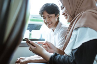 Gülümseyen genç bir Müslüman çift cep telefonu ekranına birlikte bakıyor.