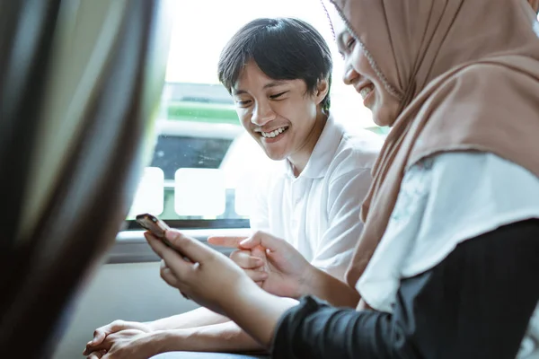 Ett leende ungt muslimskt par tittar på mobilskärmen tillsammans — Stockfoto