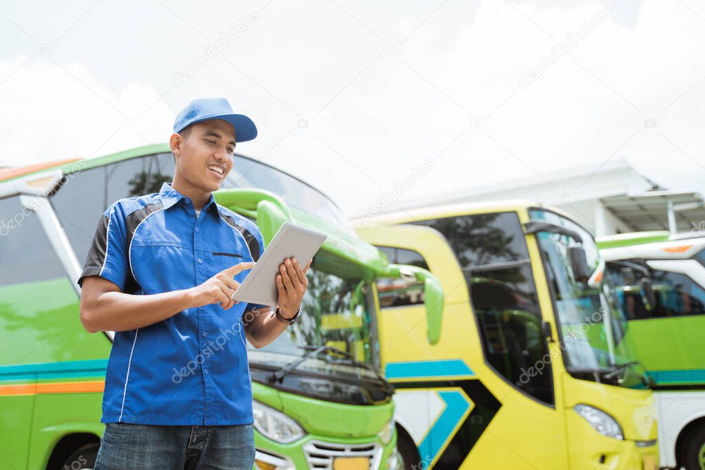 a male bus crew member in uniform and a hat smiles while using a pad