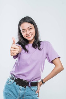 Beyaz arka planda gülümseyen güzel Asyalı genç kız modeli başparmaklarını gösteriyor