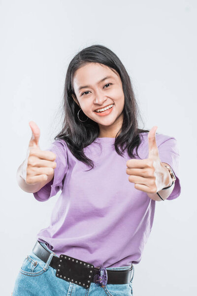 Beautiful young Asian girl model smiling on white background showing two thumbs