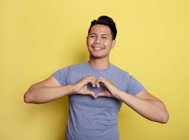 Sıradan bir genç adam gülümsemesi. Elleriyle aşk işareti.