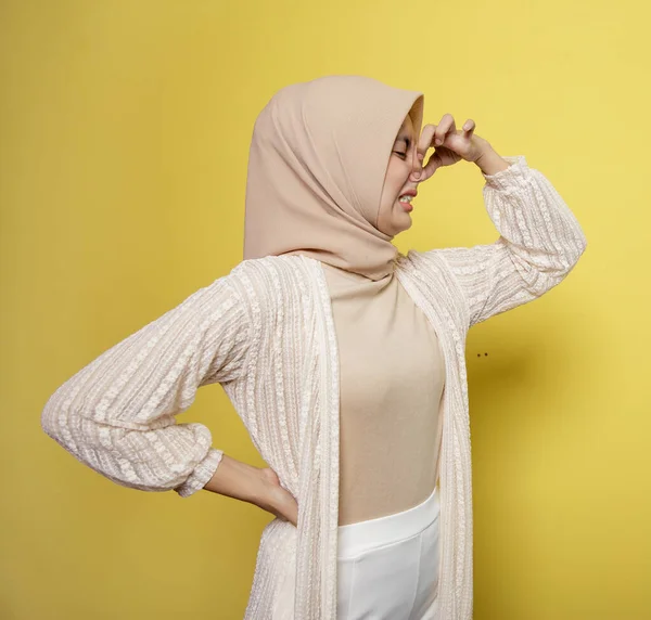 Mujer joven que usa hijab con una expresión olorosa sosteniendo una nariz — Foto de Stock