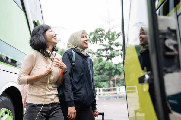 Een vrouw in een sluier met een tas kijkt naar de busdeur terwijl ze kletst en lacht met een vriendin — Stockfoto