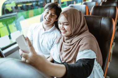 Asyalı Müslüman çiftler cep telefonu kameralarına birlikte selfie çekerken gülümserler.