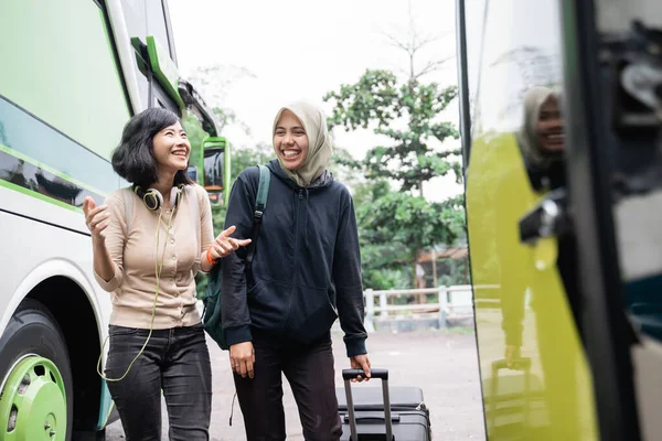 A woman in a veil with a bag and suitcase walking towards the bus while chatting with a woman moving her hands — Stock Photo, Image