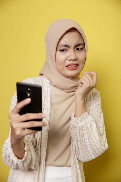 Молодая женщина носит хиджаб с выражением отвращения, глядя на ее телефон — стоковое фото