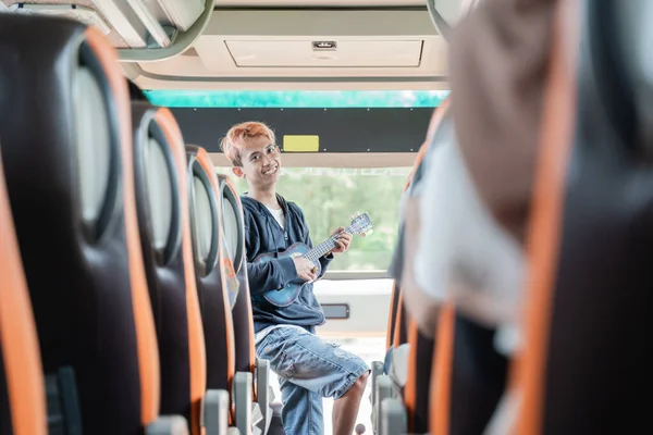 Um busker canta enquanto usa um instrumento ukulele e os passageiros do ônibus batem palmas em suas mãos — Fotografia de Stock