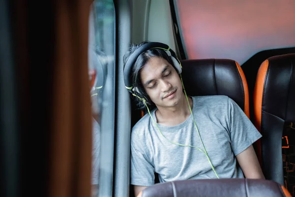Ένας νεαρός άνδρας που φοράει ακουστικά ύπνου ακουμπά στο παράθυρο ενώ κάθεται δίπλα στο παράθυρο — Φωτογραφία Αρχείου