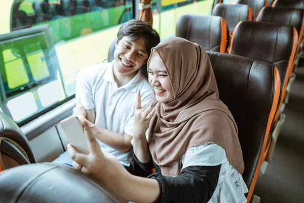 En ung asiatisk man och en ung kvinna i hijab ler mot kameran på sin mobiltelefon medan de tar en selfie tillsammans — Stockfoto