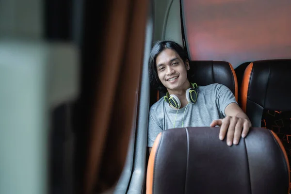 A young man in headphones smiles at the camera while sitting by a window — Stock Photo, Image