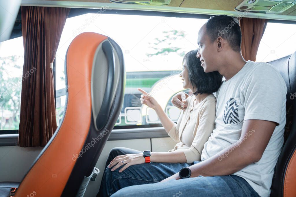 a young man and a young woman finger pointing at the window while sitting on the bus