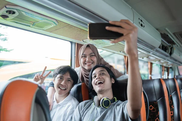 three young Asians smile and pose to their cellphone camera while taking a selfie together