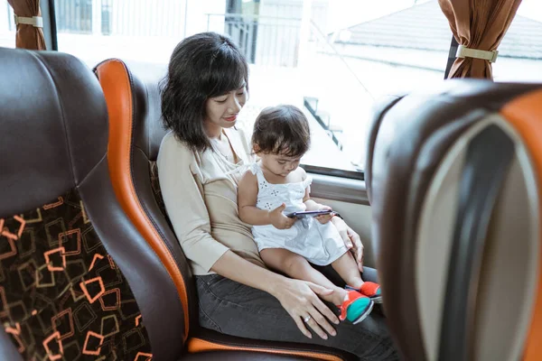 Une mère et une petite fille tenant un téléphone portable assis près de la fenêtre — Photo