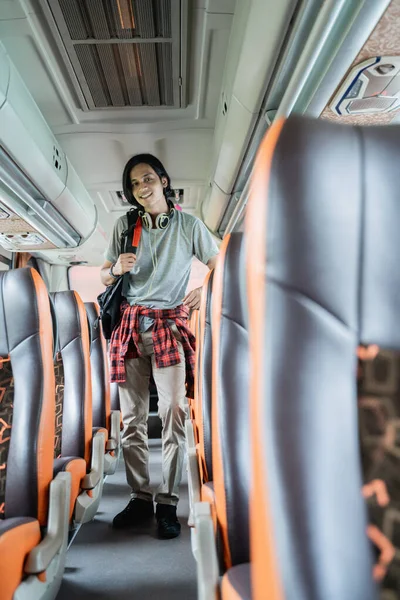 A smiling young man wearing a backpack and headphones is standing between the seats — Stock Photo, Image