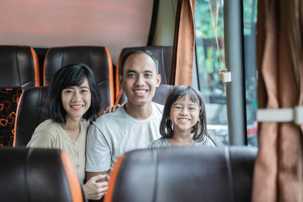 Asian mom and dad smile at the camera while cradling their daughter while sitting on the bus