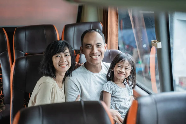 Мама і тато посміхаються на камеру, коли вони на колінах своїх дочок, сидячи в автобусі — стокове фото