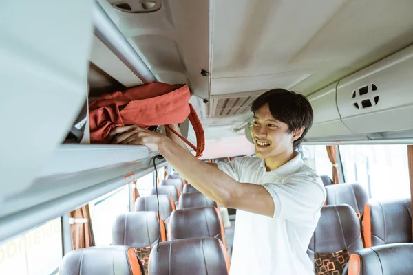 An Asian boy puts his bag on the shelf while standing