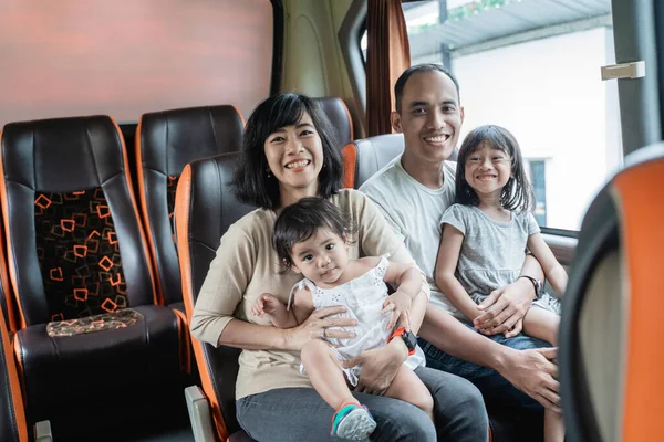 Азійська мама з татом посміхаються перед камерою, коли забирають своїх двох дітей на автобусному сидінні. — стокове фото