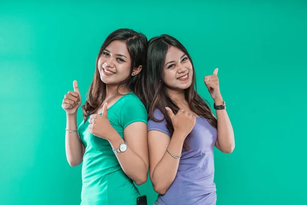 Portrait of young girls twins nice charming cheerful while showing thumbs to the camera — Stock Photo, Image