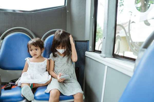 Две маленькие девочки, сидящие на скамейке и играющие на мобильном телефоне в автобусе — стоковое фото