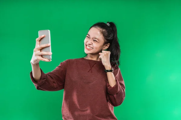 緑の背景に幸せな表情を持つ携帯電話で何かを見て肖像画の美しい若い女性 — ストック写真