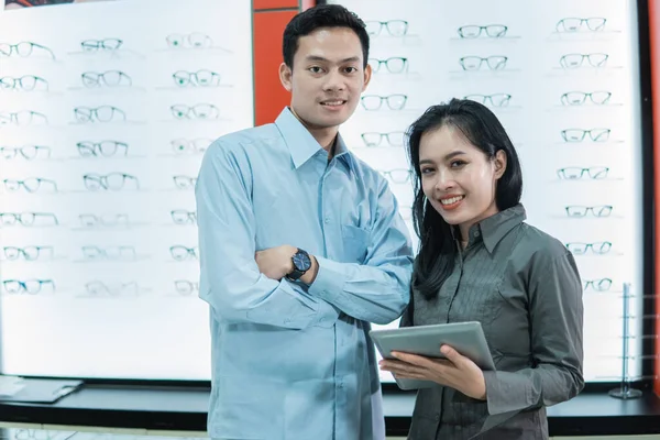 Un propriétaire de magasin de lunettes homme et femme tenant une tablette debout sur le fond d'une vitrine — Photo