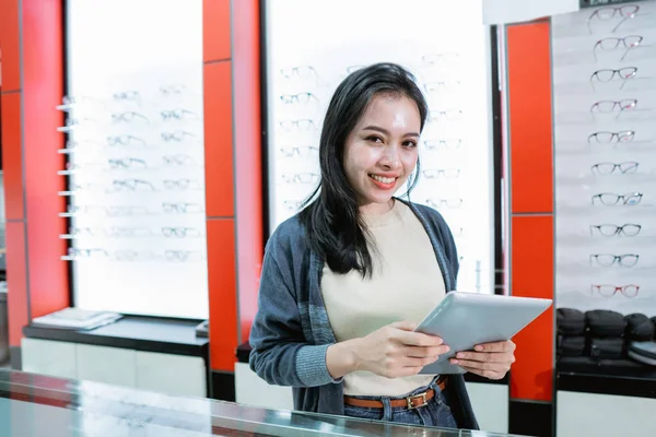 Una hermosa mujer sonriente está en una clínica ocular sosteniendo un catálogo de productos de gafas —  Fotos de Stock