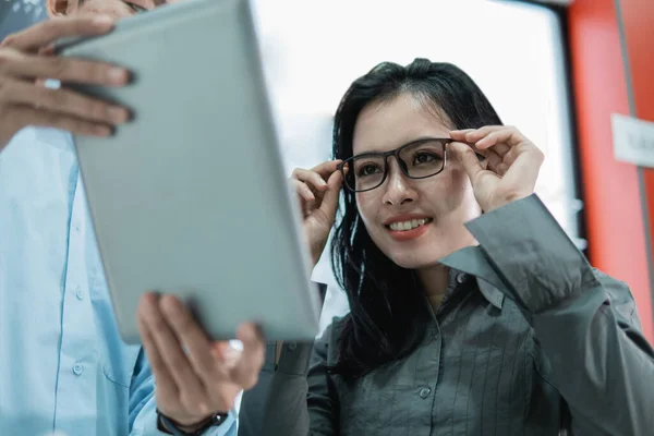 Kobieta klient próbuje na okulary, aby spojrzeć na ekranie tabletu — Zdjęcie stockowe
