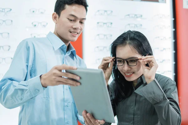 Prodavačka obsluhující zákaznici, která si zkouší brýle, aby se při stání podívala na obrazovku tabletu — Stock fotografie
