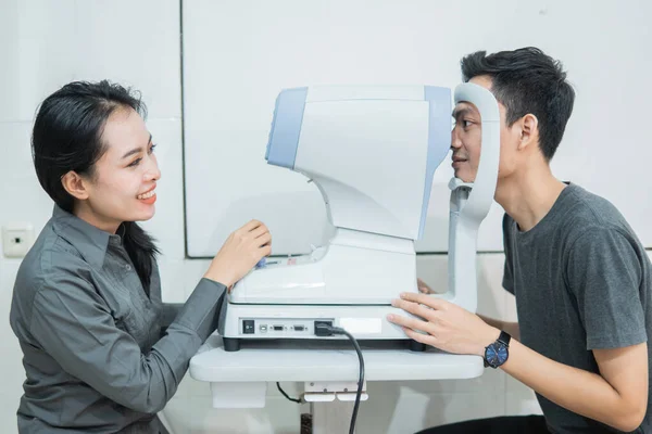 女性医師と男性患者が装置を使って目の検査を行い — ストック写真
