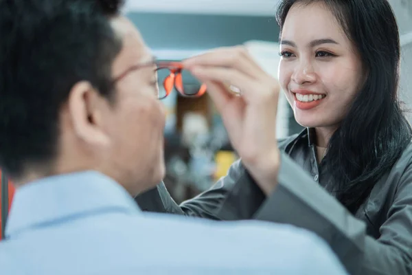 Een mooie winkelbediende helpt zetten nieuwe bril op een mannelijke klant — Stockfoto