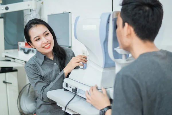 En kvinnlig läkare och en manlig patient som gör en ögonkontroll med hjälp av en anordning — Stockfoto