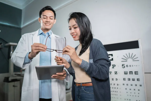 Lekarz płci męskiej podaje kobiecie wyniki analizy i pokazuje zalecane okulary do stosowania po sprawdzeniu — Zdjęcie stockowe