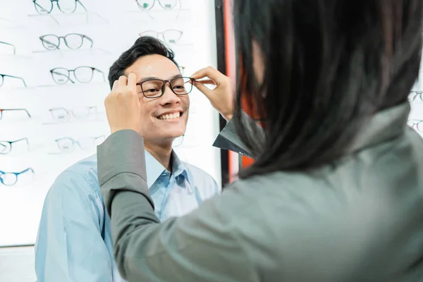 Μια γυναίκα υπάλληλος καταστήματος βάζει γυαλιά σε έναν αρσενικό πελάτη — Φωτογραφία Αρχείου